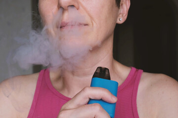Close up of middle aged woman exhaling dense vapor through nose while holding blue vape device, strong message about nicotine addiction, respiratory risks, public health and anti vaping campaigns