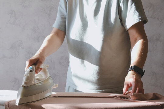 Adult in soft t shirt ironing clothes on board in warm sunlight at home, close up of hands smoothing fabric, everyday housework, cozy domestic lifestyle, cleaning and laundry service themes
