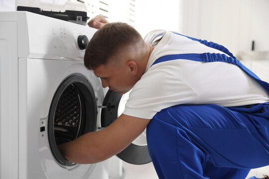 Repairman in uniform fixing broken washing machine at home