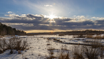 Field of snow with a sun shining through the clouds