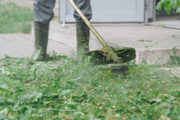 man mows green grass with trimmer, cropped, no face
