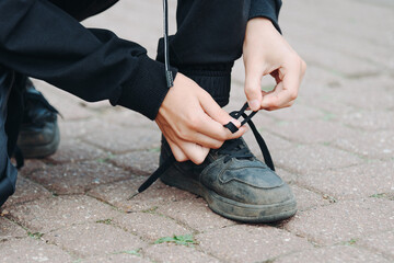 young boy ties shoelaces on his foot, black boots. closeup view, cropped, no face
