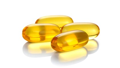 Gleaming, translucent, golden-yellow softgel capsules clustered atop a reflective white surface, creating a bright, clean display