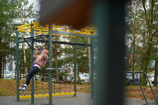 Young Woman Exercising on Monkey Bars with Resistance Band Outdoors
