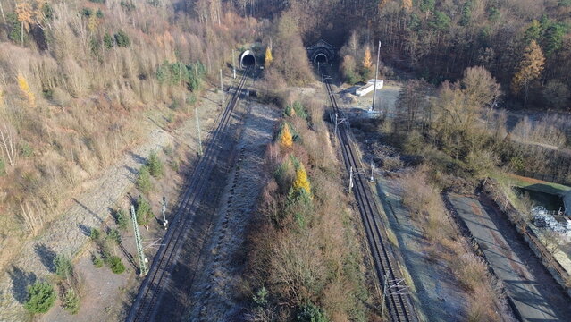 Aerial view of dual railway tunnels and frosty winter tracks surrounded by forest and rugged terrain