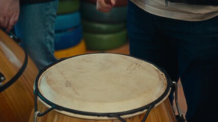 Close-up of a person playing a leather drum with a mallet, highlighting the texture of the instrument and the rhythmic hand movement in an indoor environment.