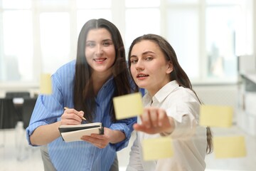 Obraz premium Colleagues discussing strategy near glass board sticky notes in office