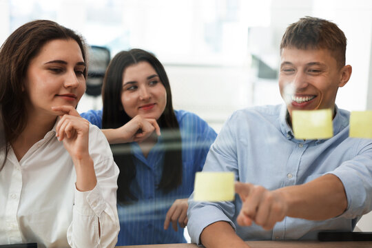 Colleagues discussing strategy near glass board sticky notes in office - Powered by Adobe