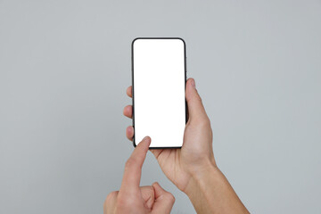 Man holding smartphone with blank screen on grey background, closeup