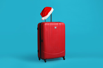 Christmas vacation. Suitcase with red Santa hat on light blue background