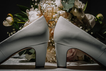 Elegant white high-heeled shoes positioned with a wedding ring nestled between them, surrounded by...