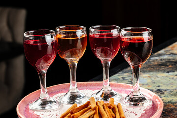 A tray elegantly presenting three small glasses of vibrant red liquid alongside golden crispy French fries for a visually appealing snack.
