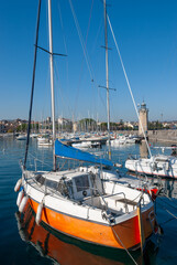 Fototapeta premium Colorful sailboats docked in the Desenzano harbor on a clear sunny day, with calm water, masts, and a stone lighthouse creating a vibrant lakeside atmosphere.