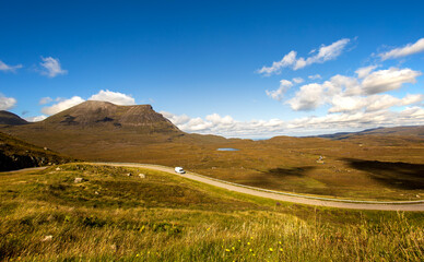 Empty single lane road with one distant car leading through the most desolated moors of the northern Scotland around Little Assynt.