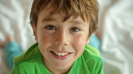 Brightly smiling young boy with brown hair and eyes in a green shirt on a white background