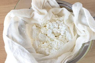 Fresh homemade cottage cheese (curd) drains through cheesecloth. Traditional dairy preparation.