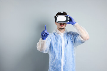 Modern technology. Doctor in headset using virtual screen on grey background. Space for text