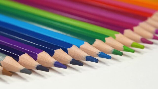 Beautiful new pencils of different colors lie on the white table. Multi-colored pencils of rainbow colors