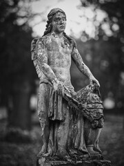 Weathered stone angel holding an urn at Goat Gate Cemetery in Bratislava, photographed in black and white.