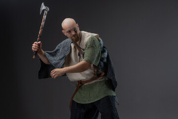 Charismatic bald man as Viking warrior holding axe and shield with fur cloak. in a fighting pose