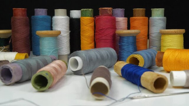 Beautiful multi-colored spools of thread lie on white table and rotates