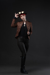 Stylish young woman in steampunk outfit, beautiful lady with short bright red hair in a bowler hat with goggles, photo on dark gray