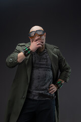 Charismatic bald man in cyberpunk raincoat with distressed fabric and head goggles.