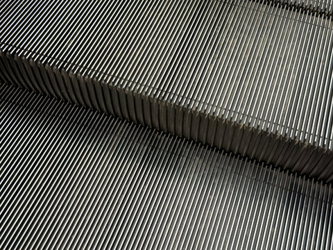 Metallic escalator steps forming an abstract pattern of parallel lines, illustrating urban movement, modern infrastructure, and continuous progress