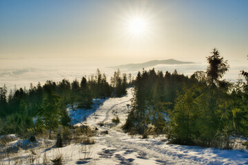 Aerial view of a snowy trail winding through a forest, with the sun casting a golden glow over the distant mountains, Spisska nova Ves, Kosicky kraj, Slovakia.