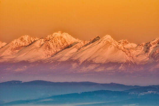 Aerial view of snow-capped peaks basking in the warm glow of the setting sun, casting long shadows over the landscape, Spisska nova Ves, Kosicky kraj, Slovakia.