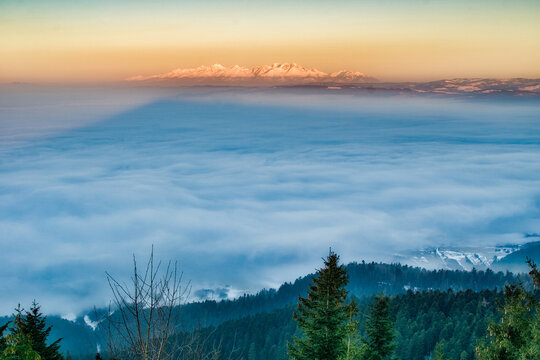 Aerial view of the majestic mountain casting a long shadow over a sea of clouds, with the forest below adding a touch of green, Spisska nova Ves, Kosicky kraj, Slovakia.