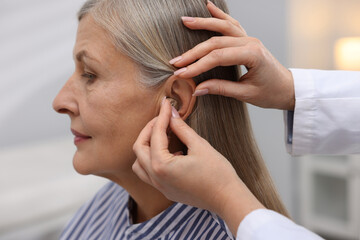 Naklejka premium Doctor putting hearing aid into patient's ear in clinic, closeup
