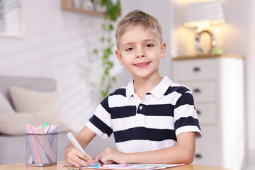 Cute little boy drawing at wooden table indoors. Space for text