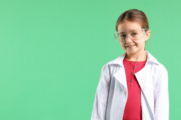 Smiling little girl in laboratory coat and protective goggles on green background, space for text. Child and science