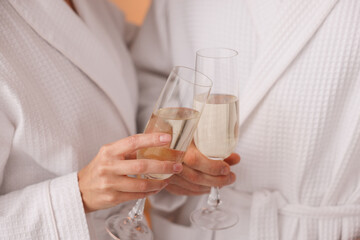 Couple in bathrobes with glasses of sparkling wine indoors, closeup