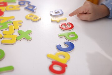 Fototapeta premium Little girl learning alphabet with letters at white table indoors, closeup