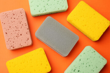 Different kitchen sponges on orange background, flat lay