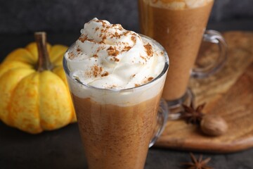 Delicious pumpkin latte with whipped cream, spices and fresh vegetable on dark table, closeup