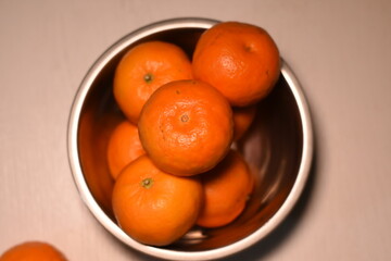 Metal bowl with tangerines on a light table, top view, vibrant fruits, minimalist background