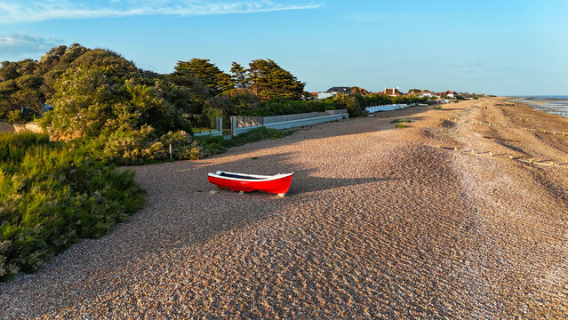 Aerial view of a solitary red boat resting on a sandy beach under the warm glow of the sun, Worthing, England, United Kingdom.