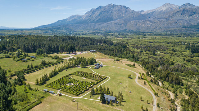Aerial view of a lush green maze nestled amidst rolling hills, framed by distant mountains under a vast blue sky, El Hoyo, Chubut Province, Argentina.