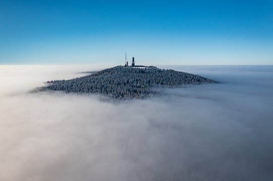 Aerial view of the frosted Grosser Feldberg peak piercing a sea of clouds under a crisp blue sky, Schmitten im Taunus, Hessen, Germany.
