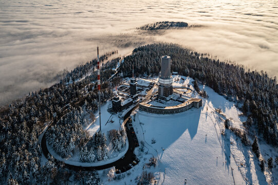 Aerial view of the snow-dusted Grosser Feldberg peak piercing through a sea of ethereal clouds, a winter wonderland spectacle, Schmitten im Taunus, Hessen, Germany.