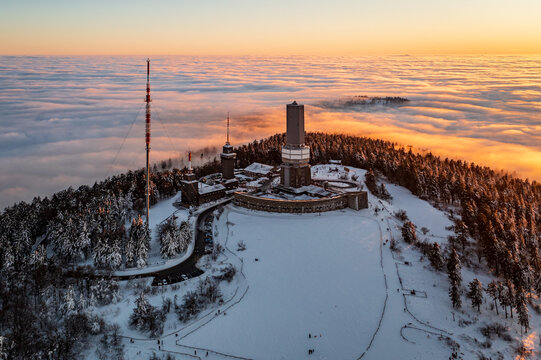 Aerial view of the Grosser Feldberg mountain peak and tower piercing through a sea of clouds at sunset, Schmitten im Taunus, Hessen, Germany.