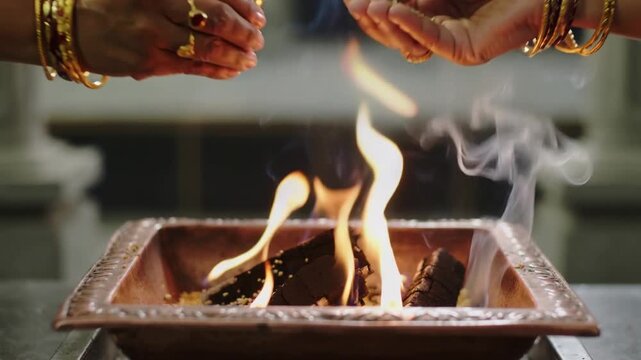 Close up hands wearing gold bangles performing a traditional religious ritual over a sacred copper fire vessel