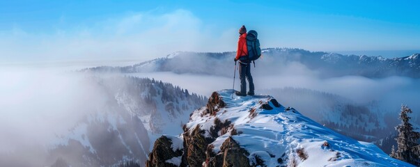 lone hiker with backpack and poles standing on snowy mountain peak above the clouds