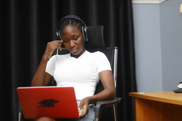 Young African lady using laptop. Woman working on computer using phone