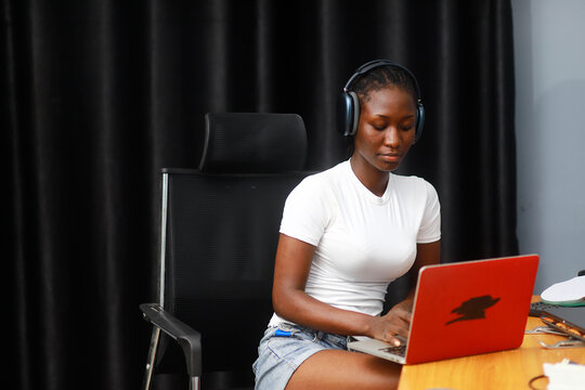 Young African lady using laptop. Woman working on computer using phone - Powered by Adobe