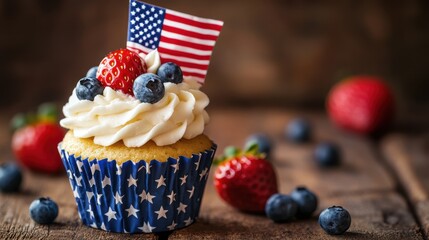 A patriotic cupcake adorned with fresh blueberries, a strawberry, and a miniature american flag, sitting on a rustic wooden surface