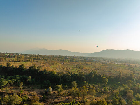 Aerial view of paragliders dancing in the sky above lush greenery and distant misty mountains, Bir, Himachal Pradesh, India.